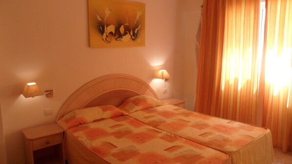 Une chambre à coucher avec un lit, deux tables de chevet, une lampe fixée au mur et un tableau.
