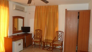 Une chambre comprenant un lit, un bureau avec une télévision, deux chaises, une armoire et un ventilateur de plafond.