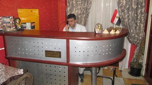 A hotel reception desk with a plaque reading "CITY PLAZA HOTEL," a telephone, and various decorative items including a golden statue and a small Egyptian artifact. - City Plaza Hostel (Cairo)