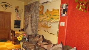 A living room with a sofa set, a table with a vase of flowers, a painting on the wall, and a red wall with a 'Tokyo' sign. - City Plaza Hostel (Cairo)