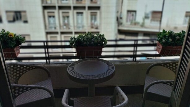 A balcony with two wicker chairs and a small round table, potted plants, and a view of buildings in the background. - City Plaza Hostel (Cairo)
