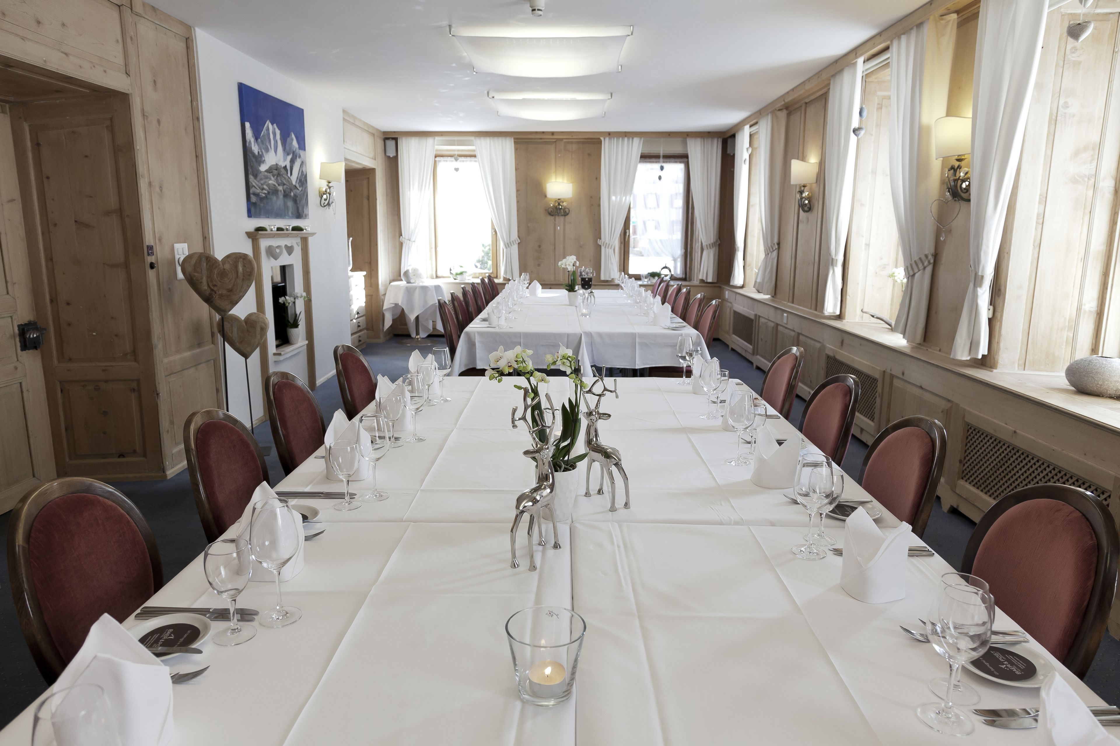 Una larga mesa de comedor lista para un evento formal, con sillas a ambos lados, manteles blancos y un centro de mesa con figuras de ciervo de plata.