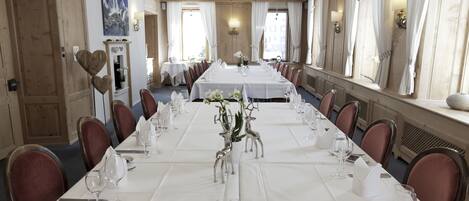 Una larga mesa de comedor lista para un evento formal, con sillas a ambos lados, manteles blancos y un centro de mesa con figuras de ciervo de plata.
