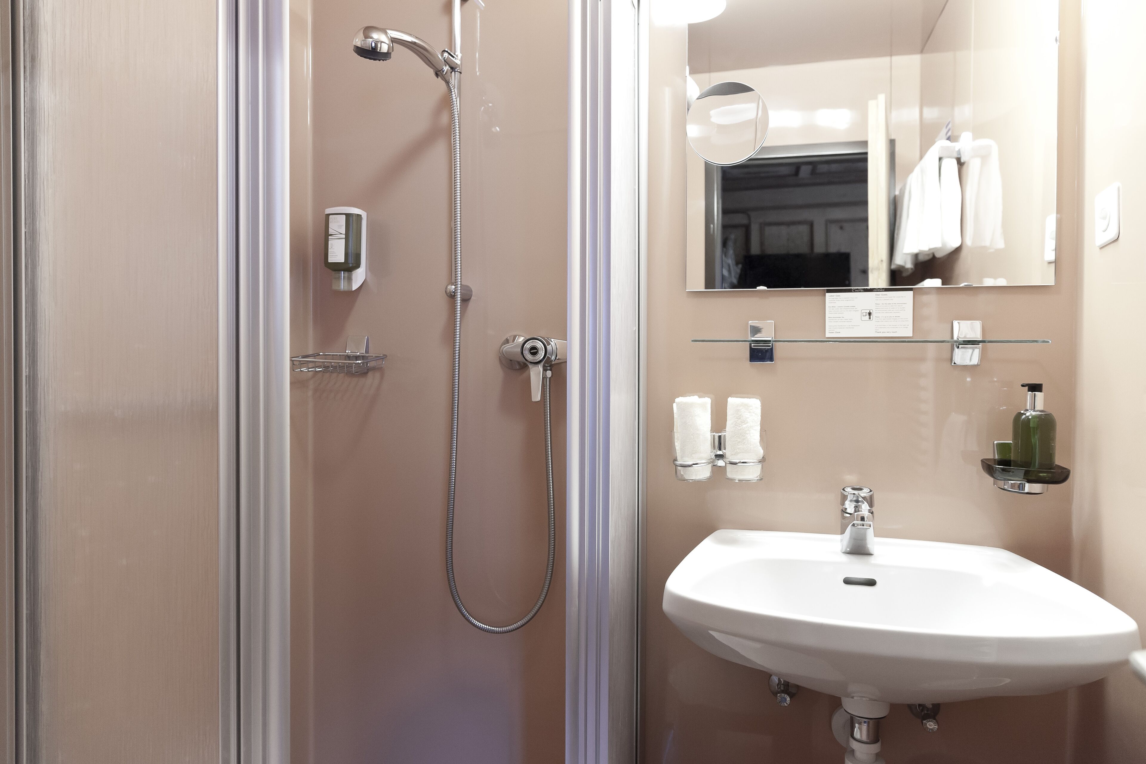Un baño moderno con cabina de ducha de vidrio, un lavamanos blanco y un espejo encima.