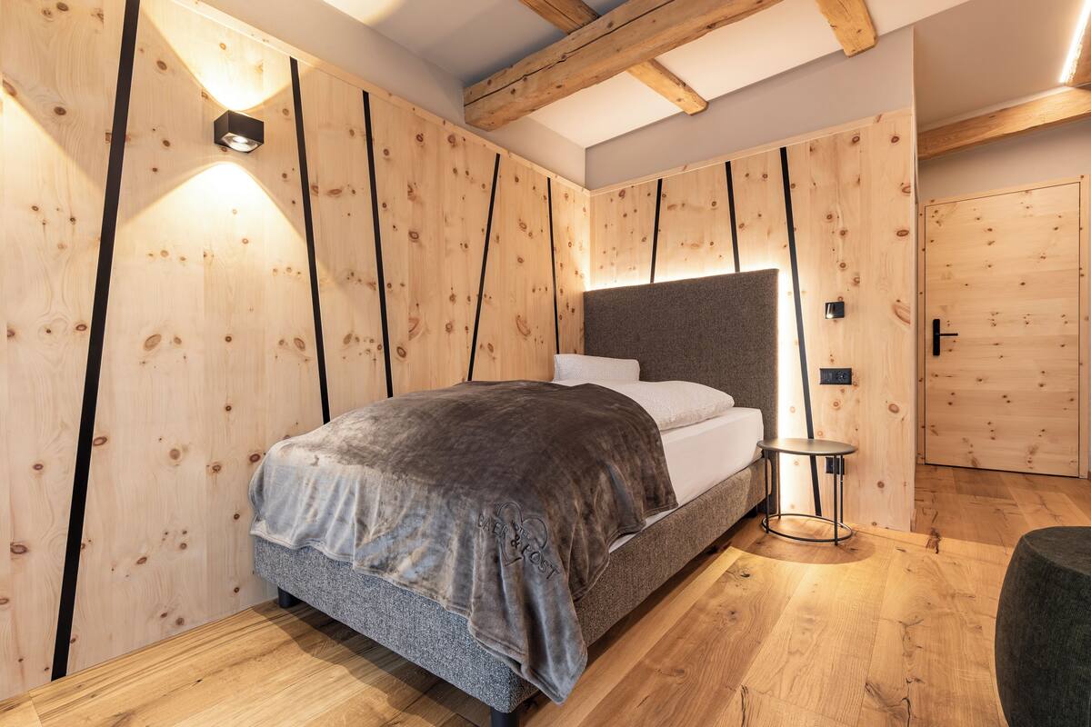 A modern bedroom with a wooden slat wall design, a bed with a grey blanket, a small round table, and a door with a handle.