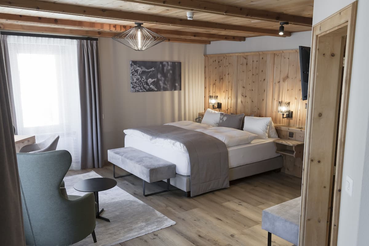 A modern bedroom with a wooden ceiling, a large bed with a grey blanket, bedside tables with lamps, and a wall-mounted TV.