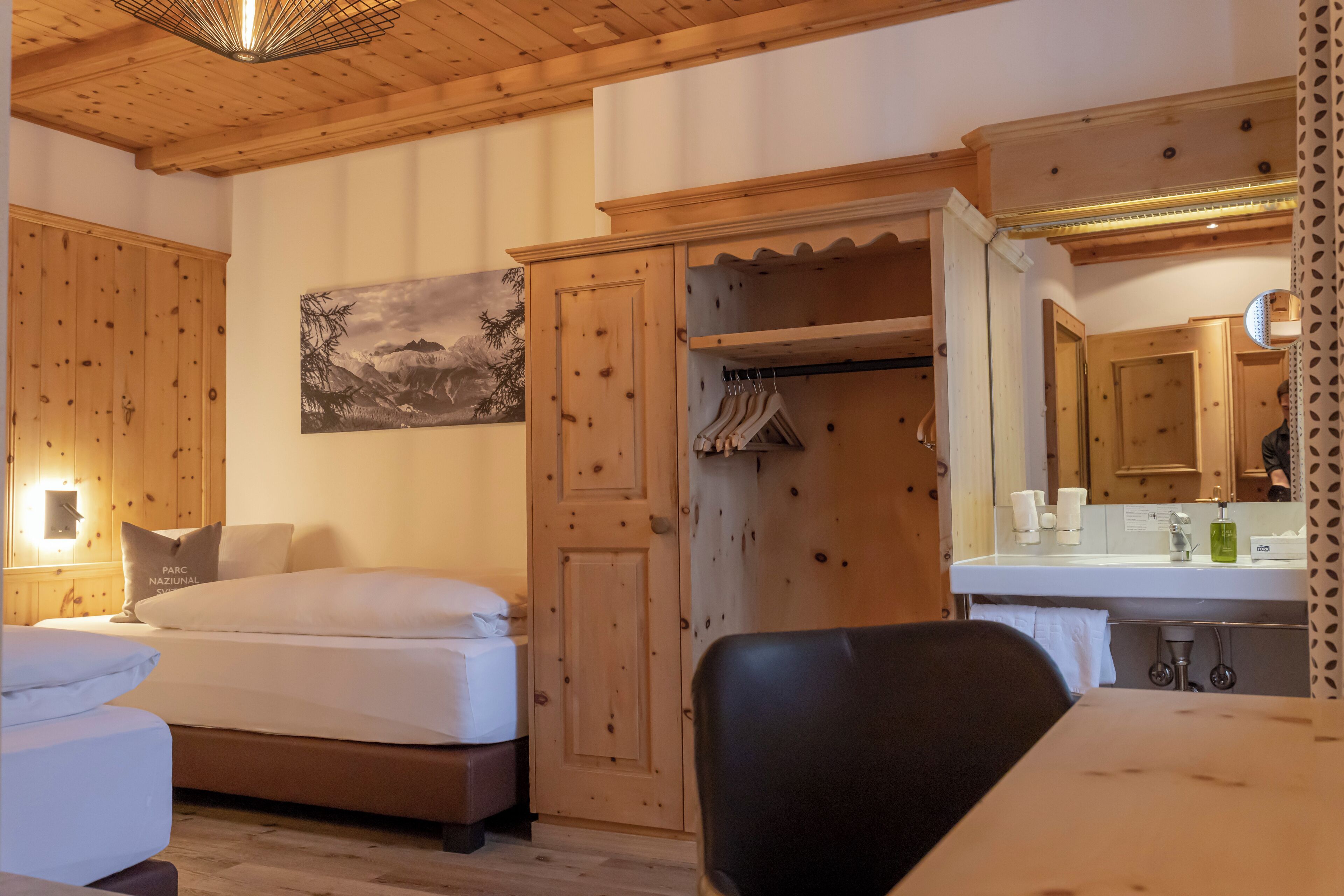 Una habitación con paneles de madera, una cama, un armario, un espejo y un lavamanos.