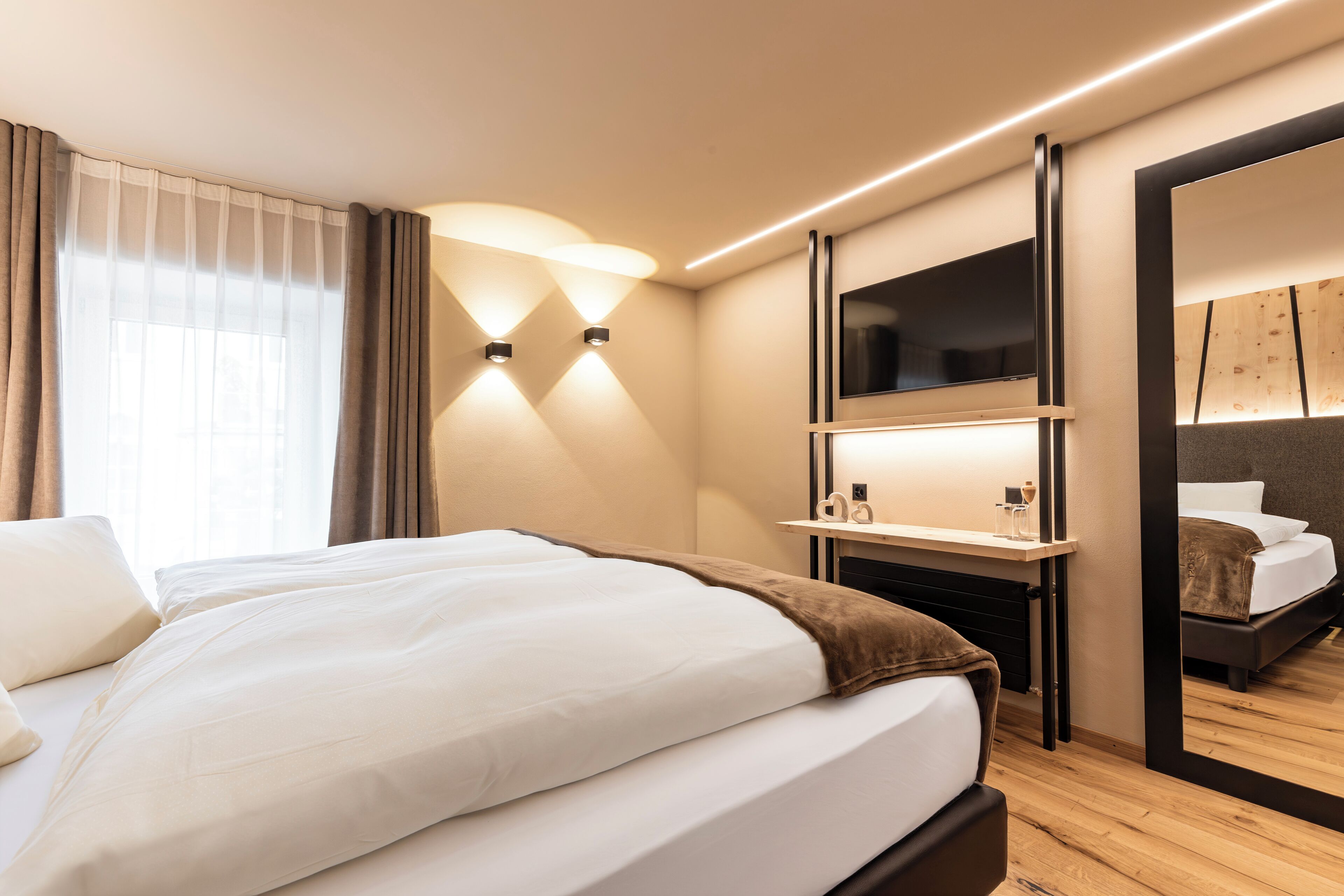 Habitació d'hotel moderna amb un llit gran, taules de nit, un mirall i una televisió.