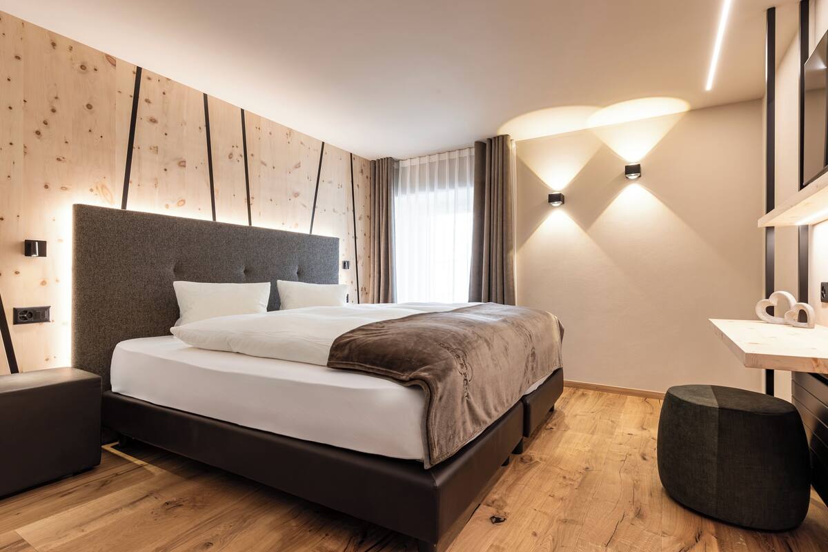 A modern bedroom with a large bed, wooden flooring, a headboard, bedside tables, and a desk with a chair.