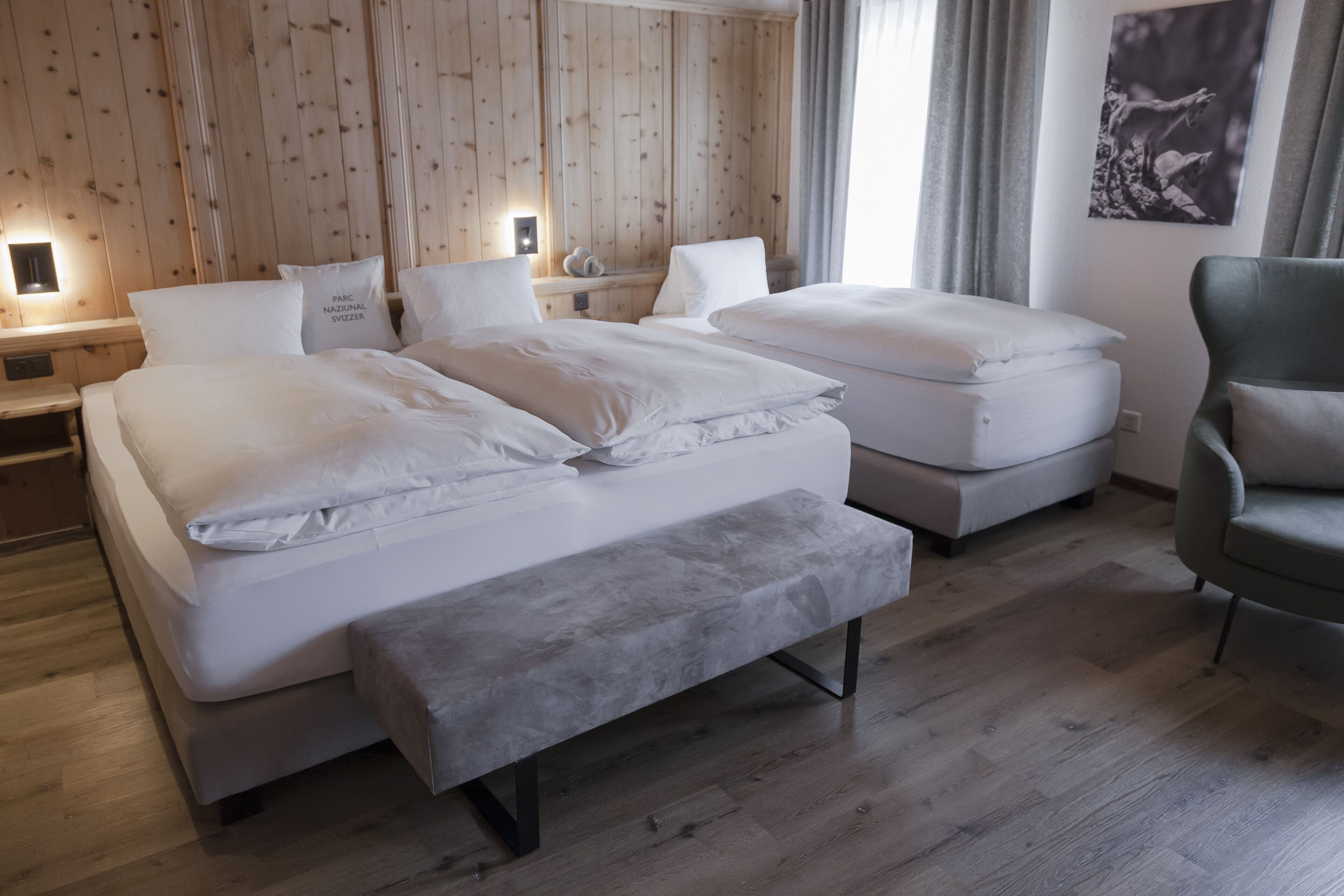 Une chambre d’hôtel avec deux lits, un banc, une chaise, des murs en bois et un tableau.