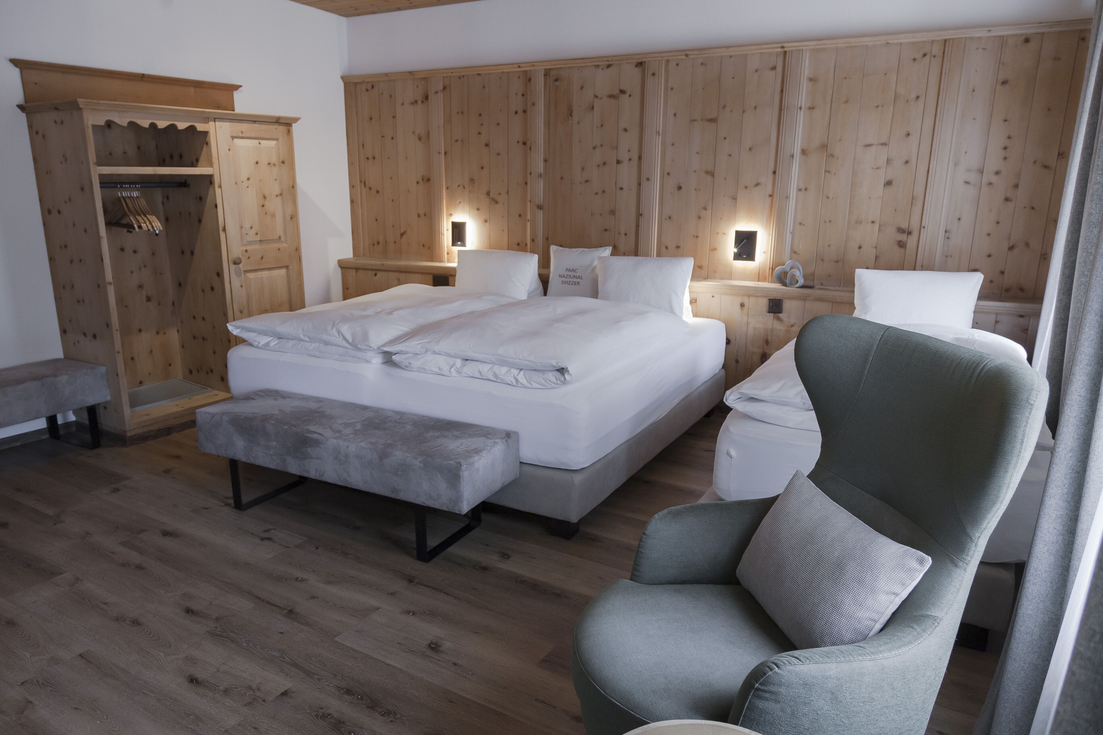Un dormitorio moderno con una cama grande, un sillón gris, un armario de madera y un banco.