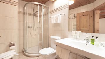 A bathroom with a glass-enclosed shower, a toilet, a sink with toiletries, and a mirror.