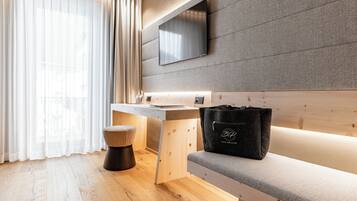 Een moderne hotelkamer met een houten bureau, een bankje, een televisie aan een gestructureerde muur en een raam met dunne gordijnen.