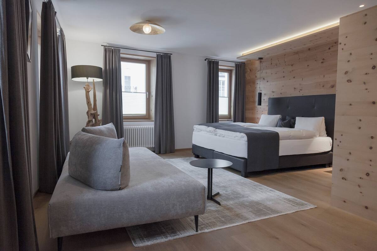 A modern bedroom with a grey sofa, a bed with white bedding, and a wooden accent wall.