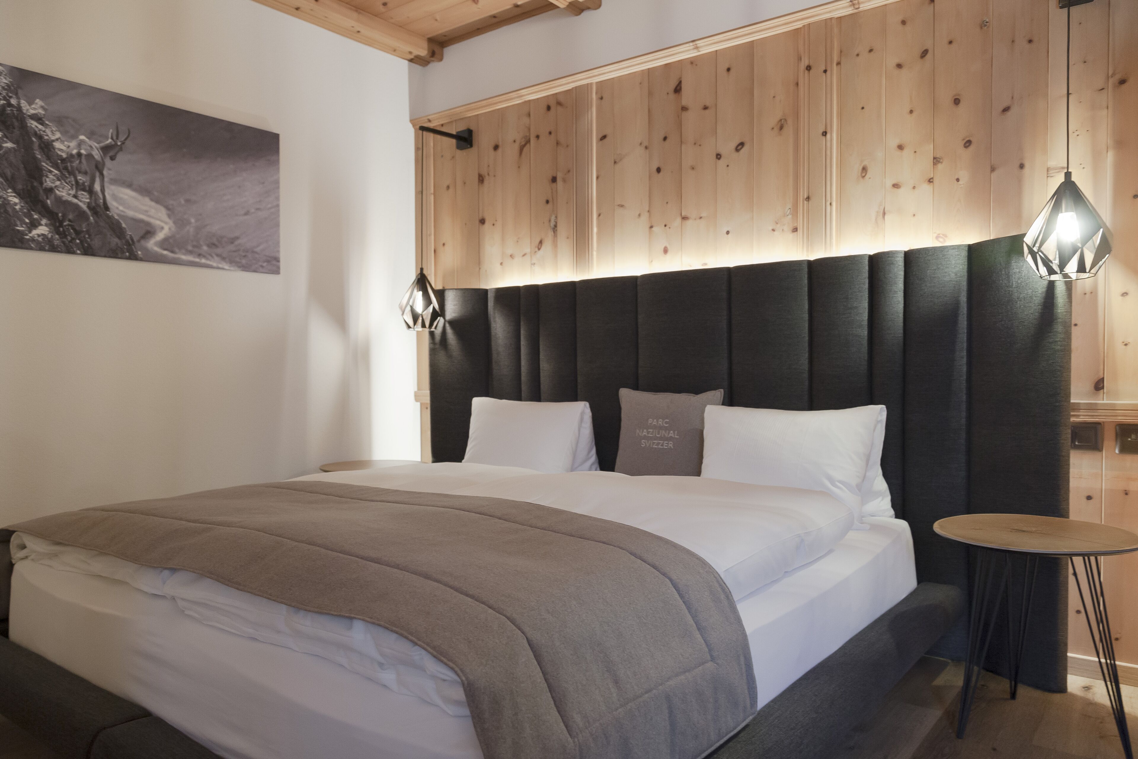 Une chambre moderne avec un grand lit, une tête de lit sombre et une petite table ronde.