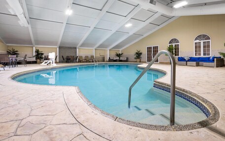 An indoor swimming pool with a tiled edge, a metal ladder, and a seating area with a sofa and chairs.