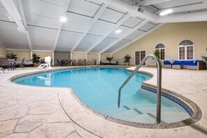 Una piscina interior con borde de azulejos, una escalera de metal y un área de estar con sofá y sillones.