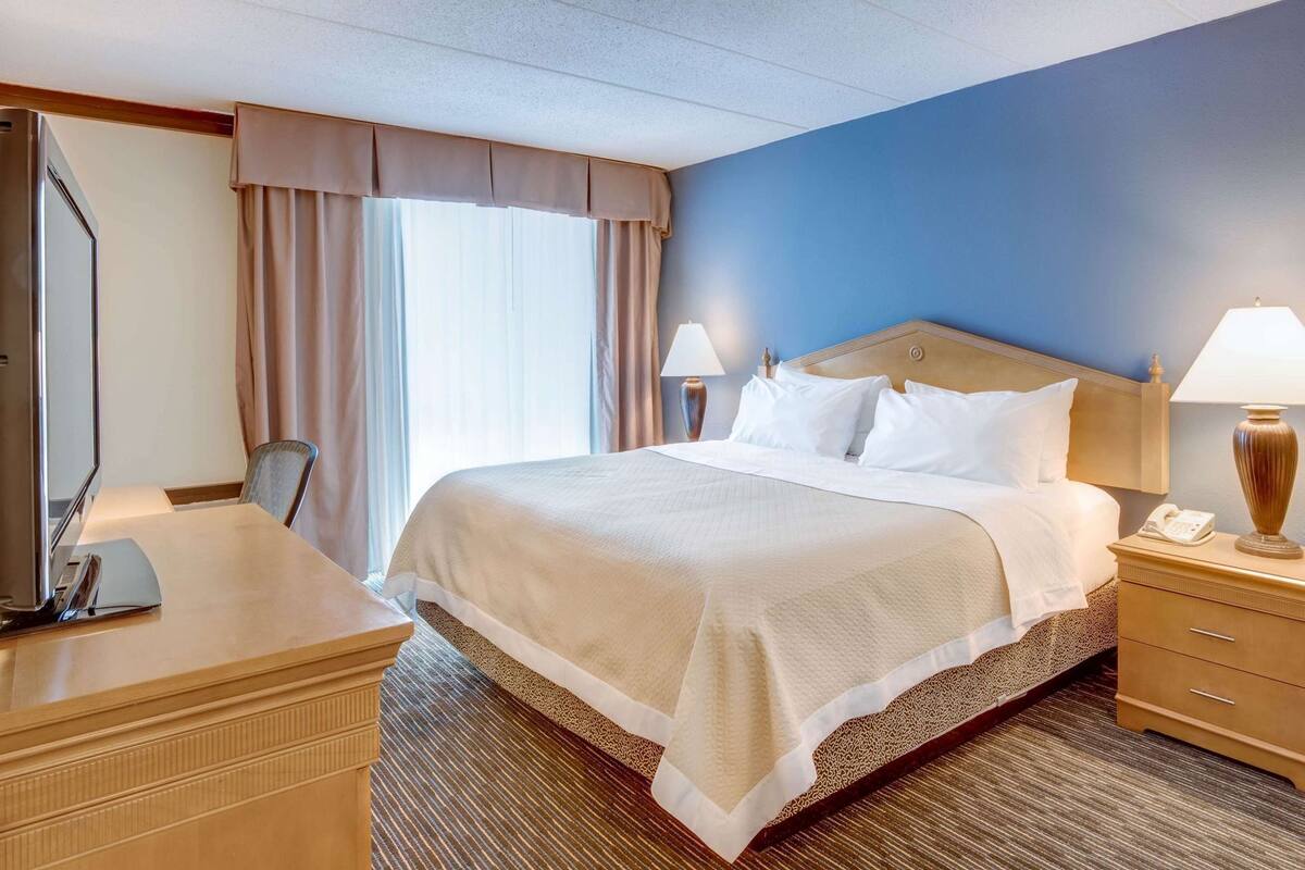 A hotel room with a bed, bedside lamps, a desk with a telephone, and a chair.