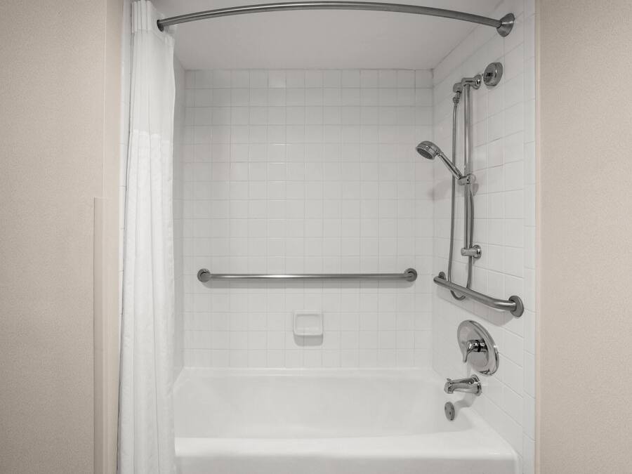 A white tiled shower with a grab bar, a handheld showerhead, and a wall-mounted faucet.