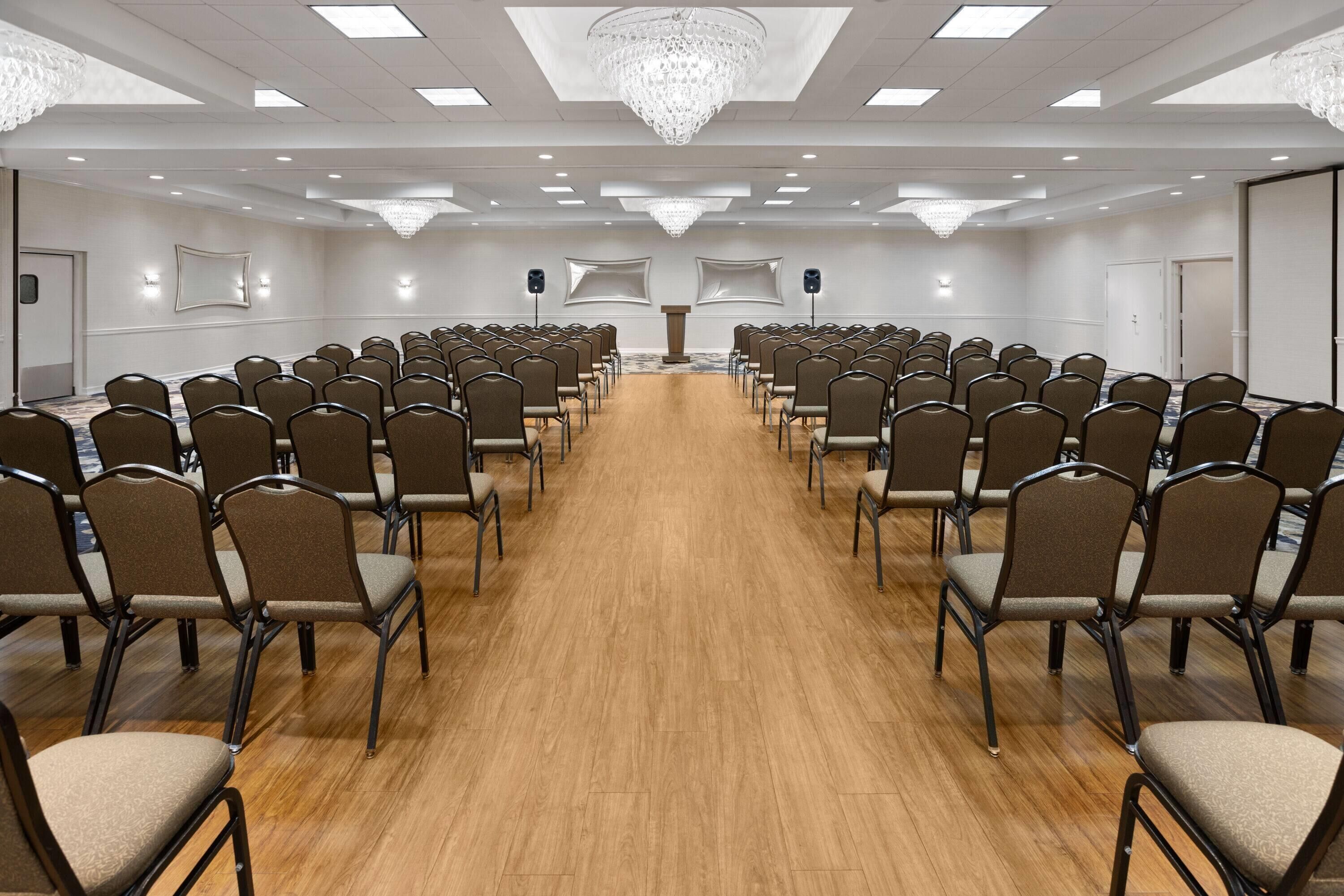 A conference room with rows of chairs, a podium, and a large chandelier.
