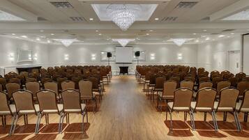 A conference room with rows of chairs, a large chandelier, and a projector screen.