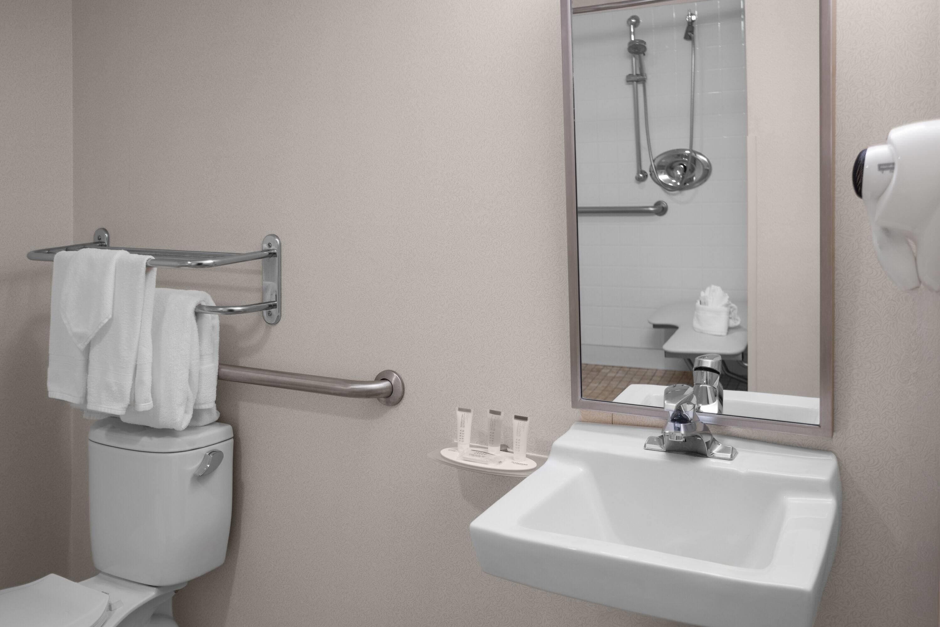 A bathroom with a toilet, a sink, a towel rack, a mirror, and a shower.