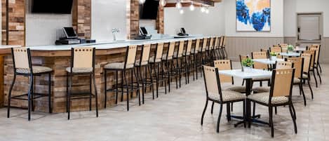 Un restaurante con una barra larga, varias sillas y un televisor en la pared.