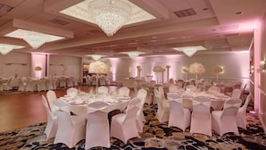 A banquet hall with round tables, white chairs, and chandeliers. - Days Hotel by Wyndham Toms River Jersey Shore (Toms River)