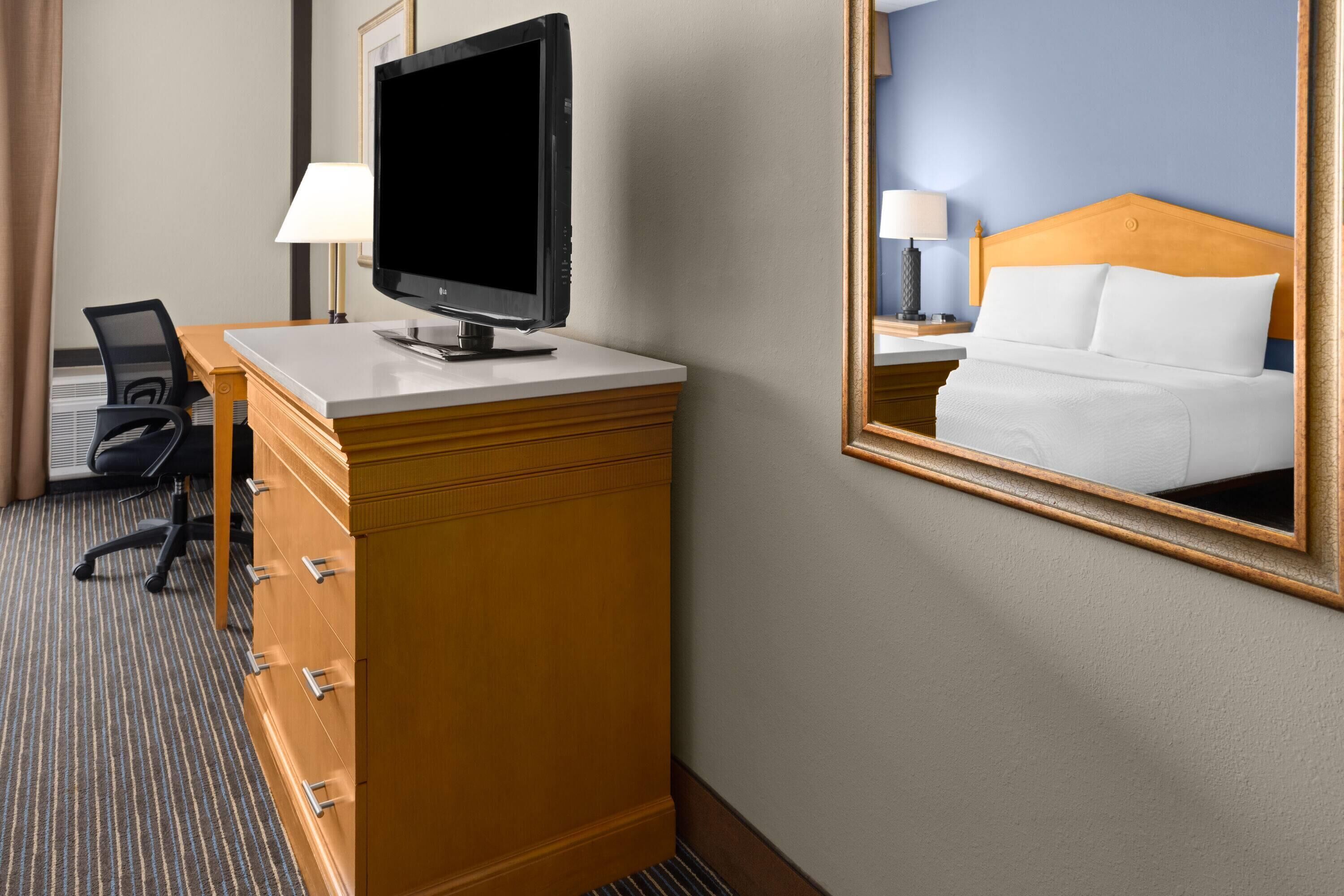 A hotel room with a desk, chair, TV, and a bed with a headboard.