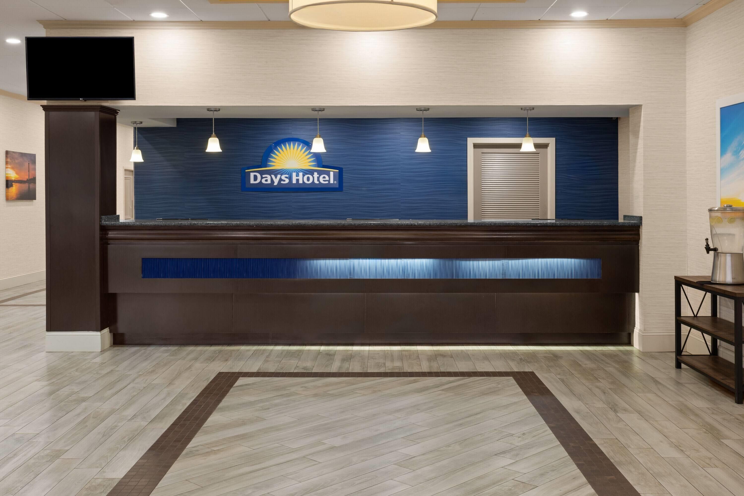Een receptiebalie met een Days Hotel bord, hanglampen, een flatscreen-tv en een vloer met een patroon.