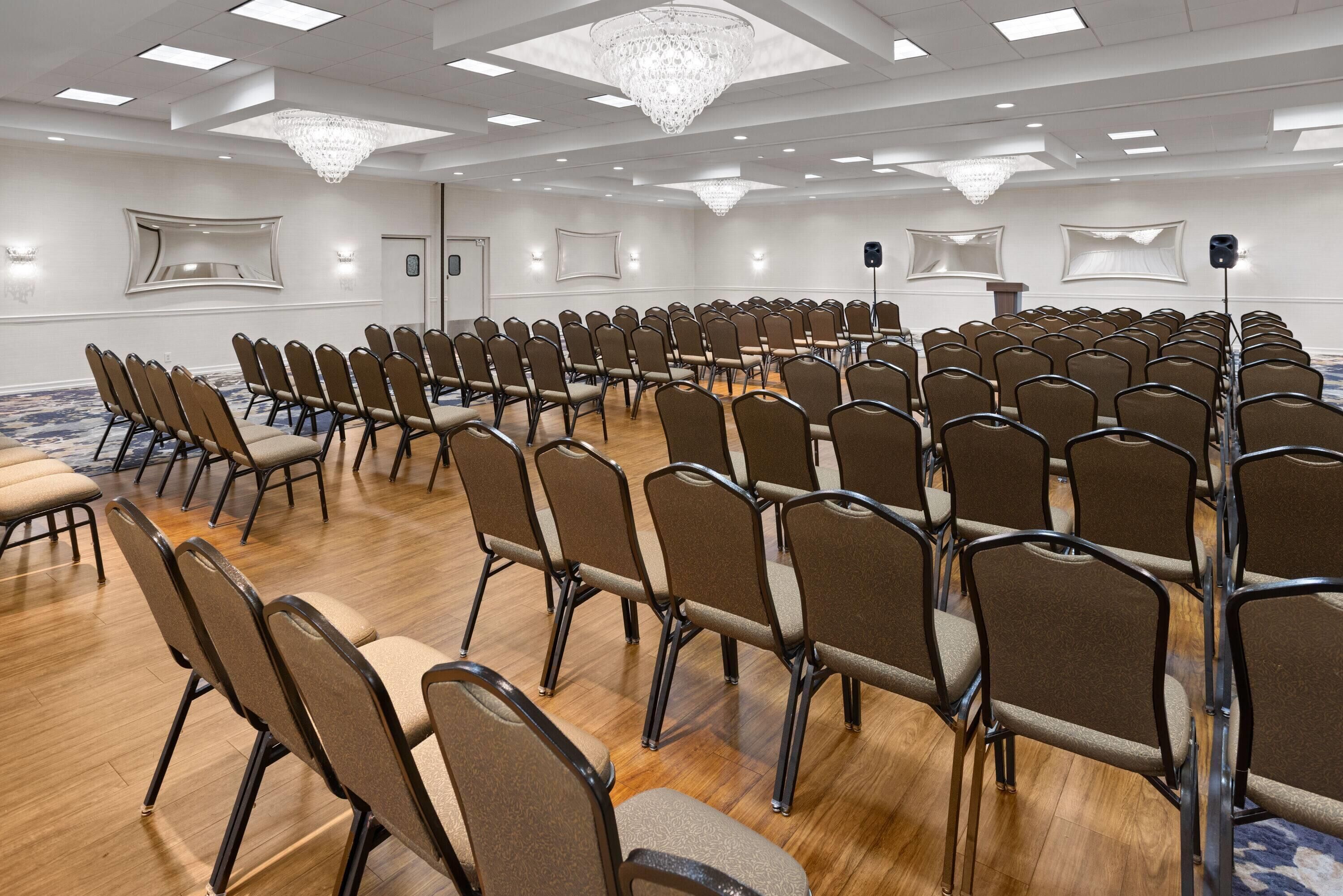 A conference room with rows of chairs, a chandelier, and a podium.