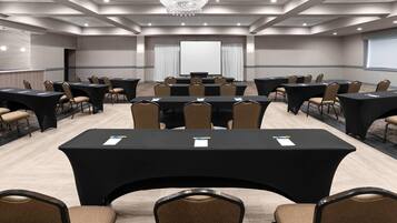 A conference room with multiple tables and chairs, a projector screen, and a chandelier.