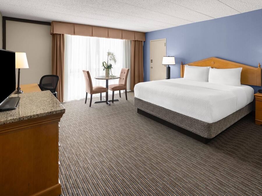 Ein Hotelzimmer mit Bett, Schreibtisch, Stuhl und einem kleinen Tisch mit Lampe.
