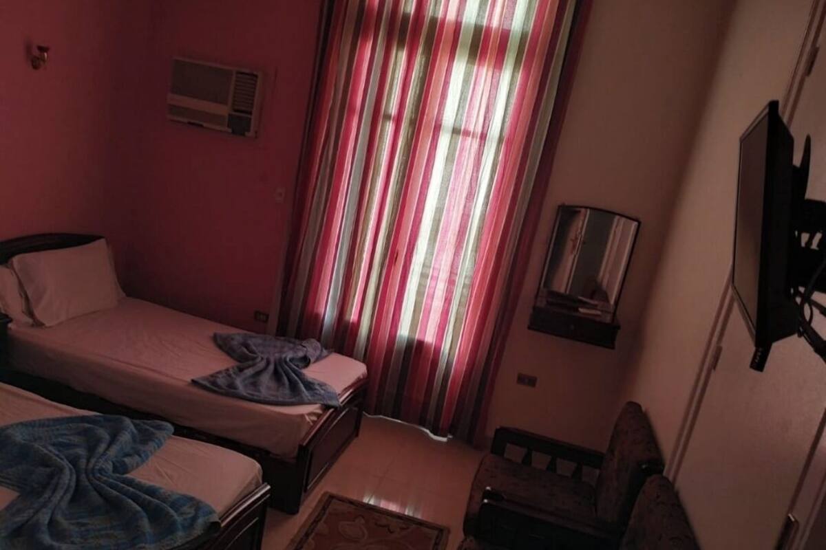 A bedroom with two beds, a TV, and a window with striped curtains.