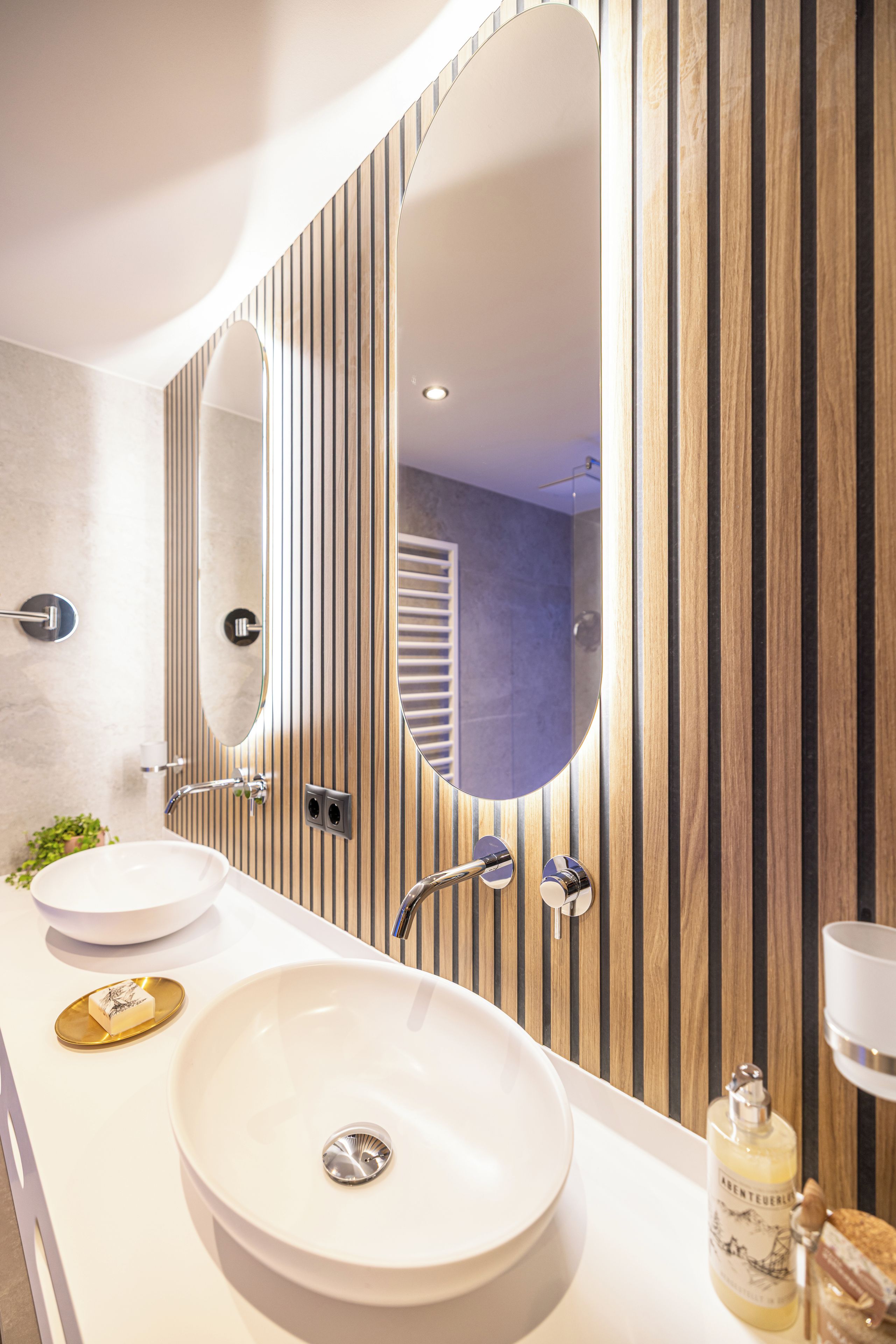 A modern bathroom with a large oval sink, a mirror, and a wooden panel wall.