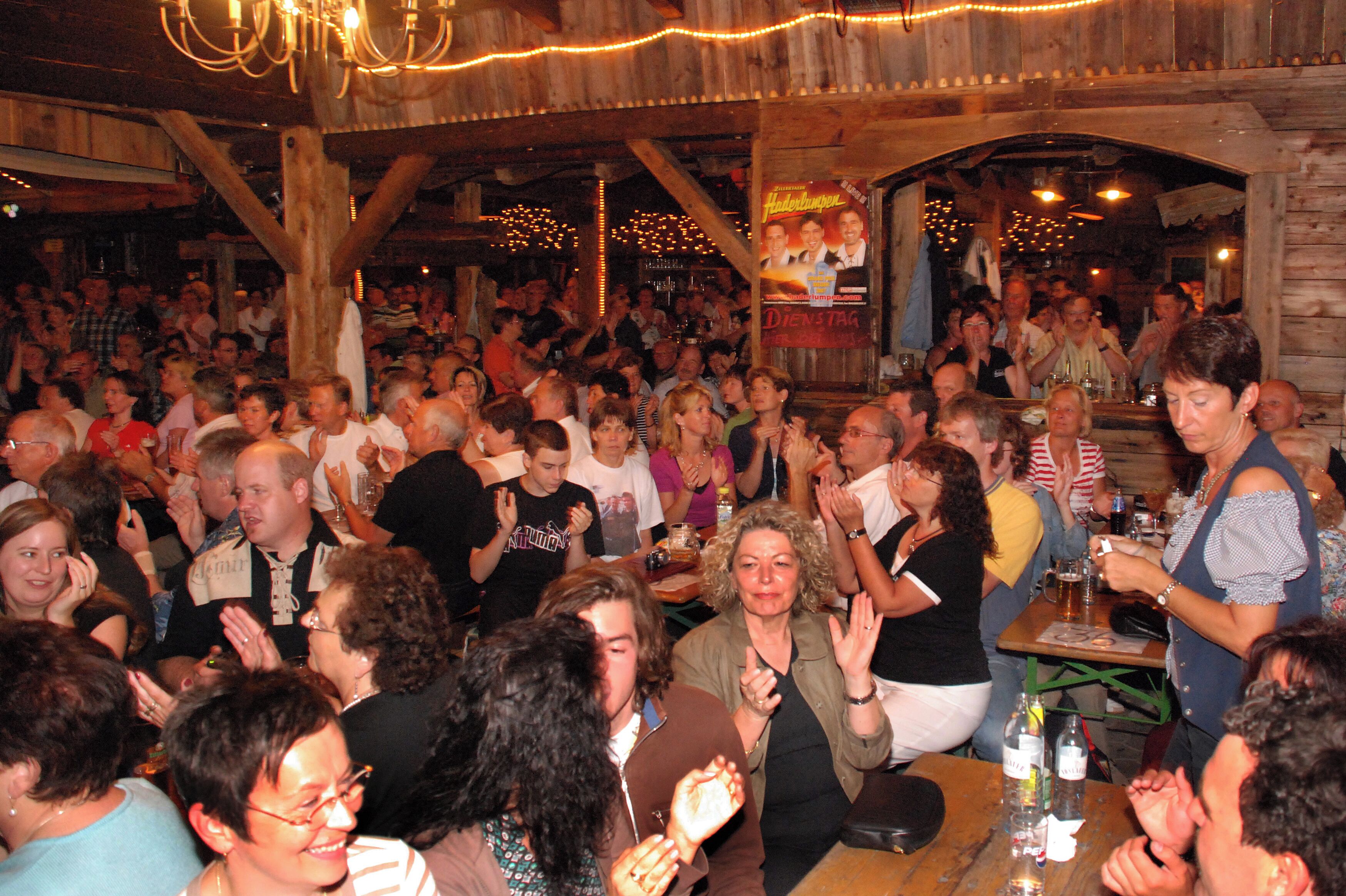 A crowded indoor venue with wooden beams, tables, and chairs.