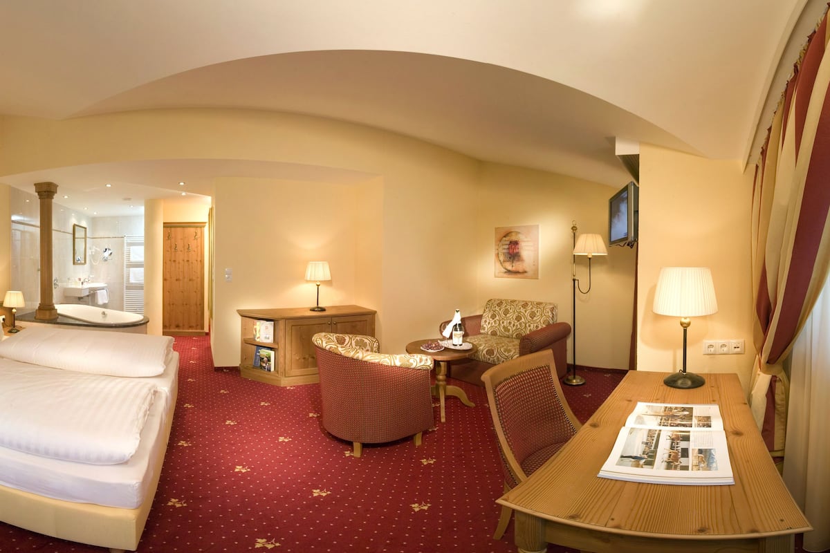 Una habitación de hotel con una cama grande, una mesita de noche de madera, una pequeña mesa con una lámpara, una silla y un televisor.