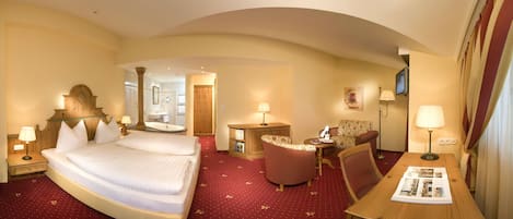 A hotel room with a large bed, a wooden nightstand, a small table with a lamp, a chair, and a television.