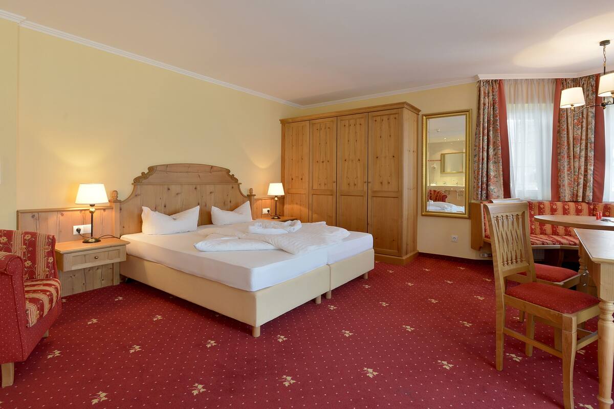 Una habitación de hotel con una cama grande, un armario de madera, una mesa de comedor con sillas y un espejo.