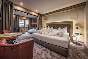 A hotel room with a large bed, a round table, a chair, and a view of the outside.