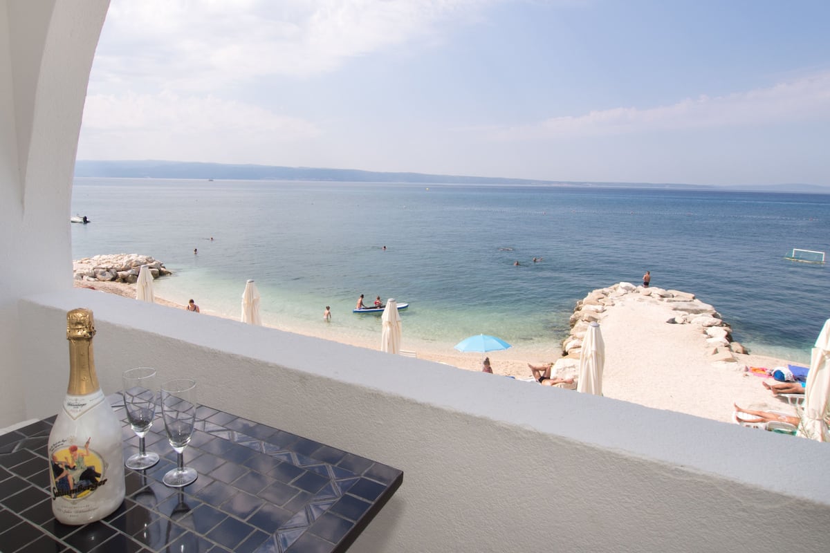 A balcony with a view of the sea, a bottle of champagne, and two glasses on a tiled table.