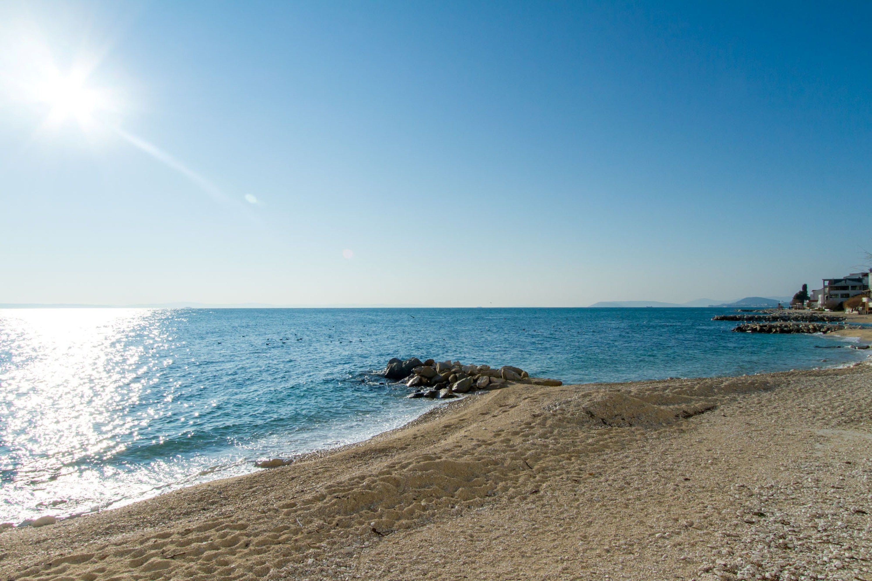 A beach with clear skies, calm water, and a rocky outcrop.