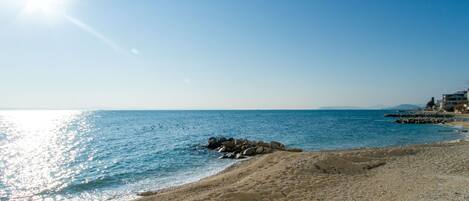 A beach with clear skies, calm water, and a rocky outcrop.