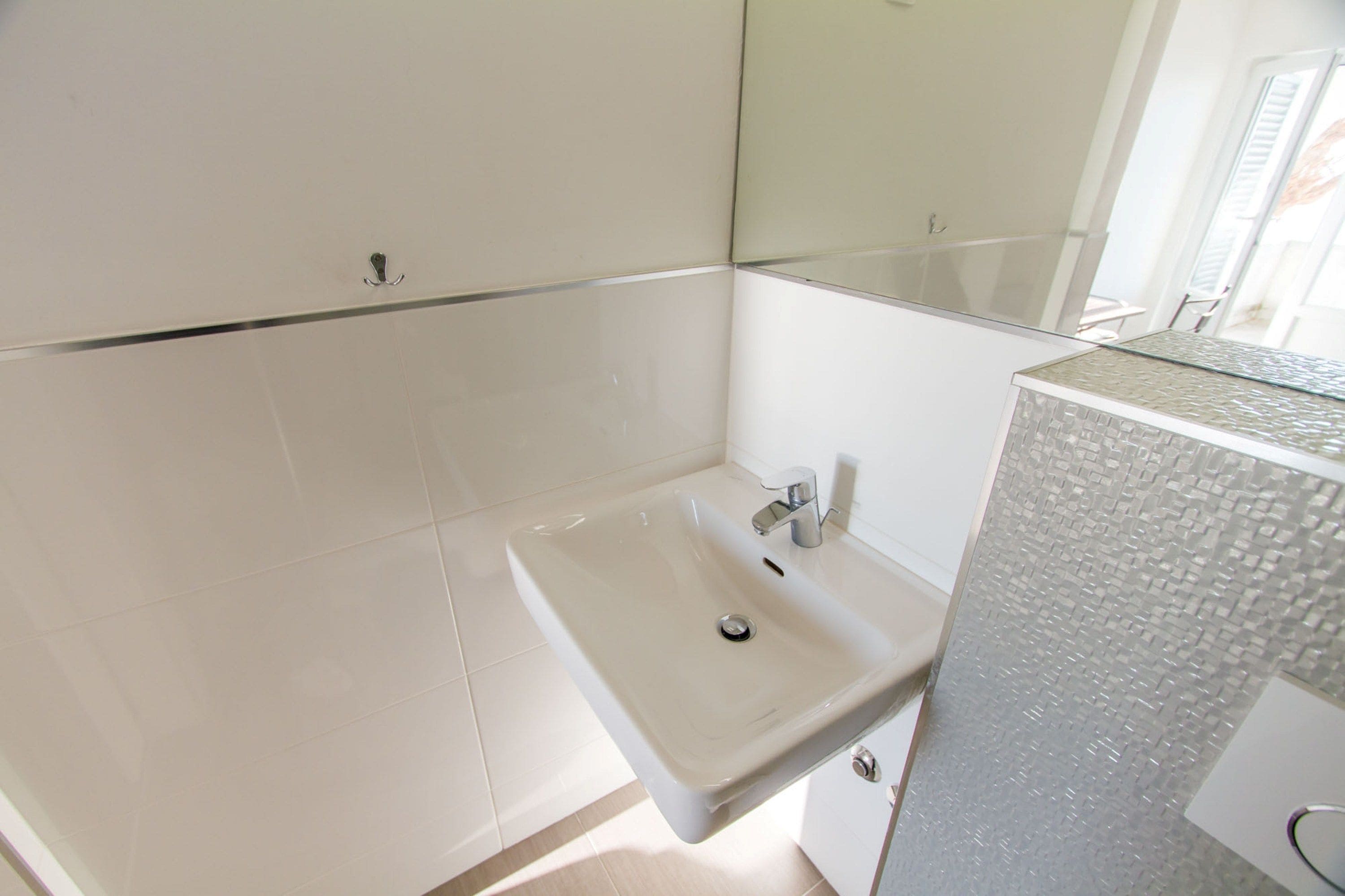 A bathroom with a white sink, a mirror, and a tiled wall.