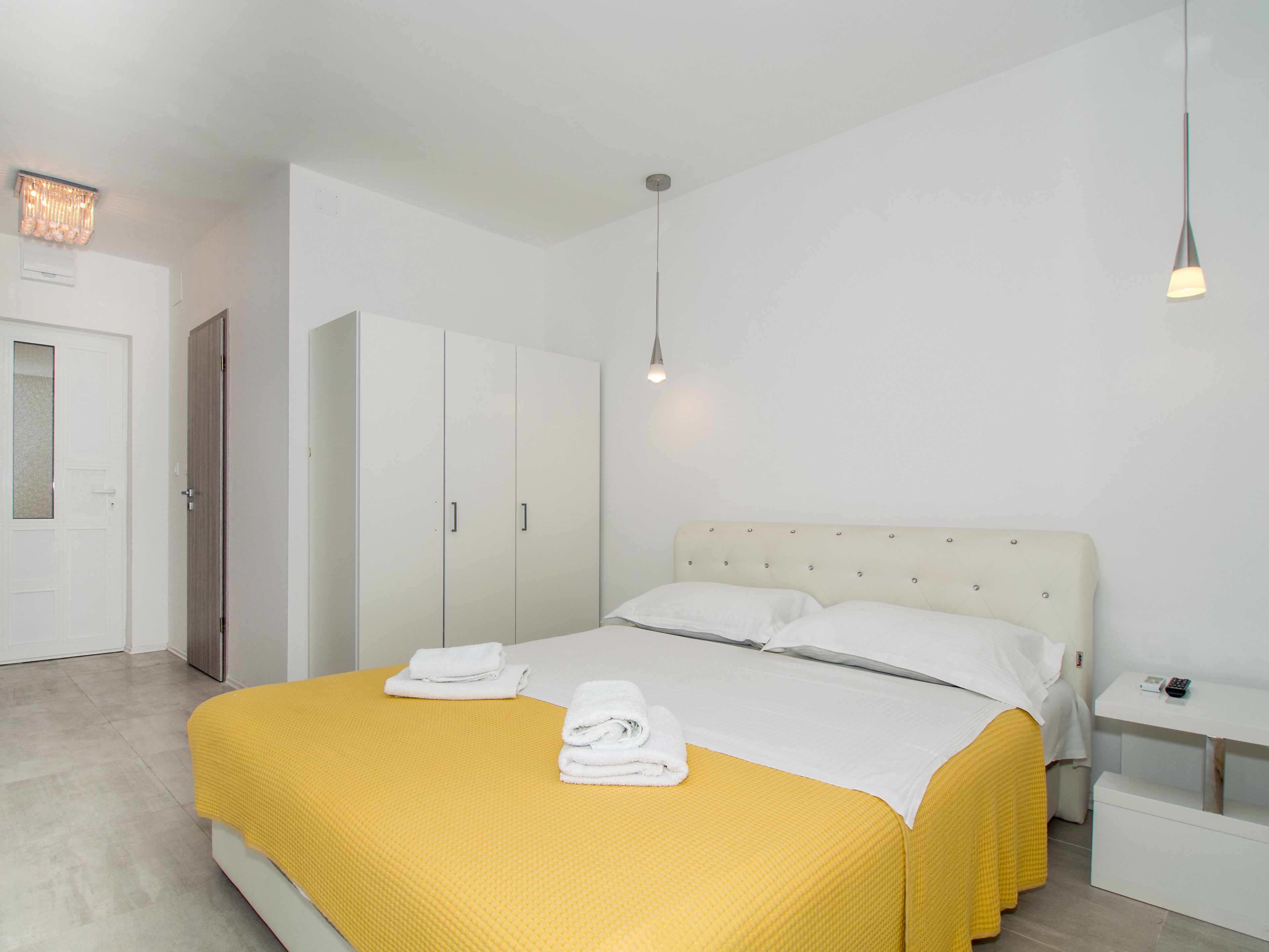 Una habitación de hotel con cama, armario, mesita de noche y lámpara colgante.