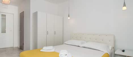 Quarto de hotel com cama, guarda-roupa, mesa de cabeceira e luminária pendente.