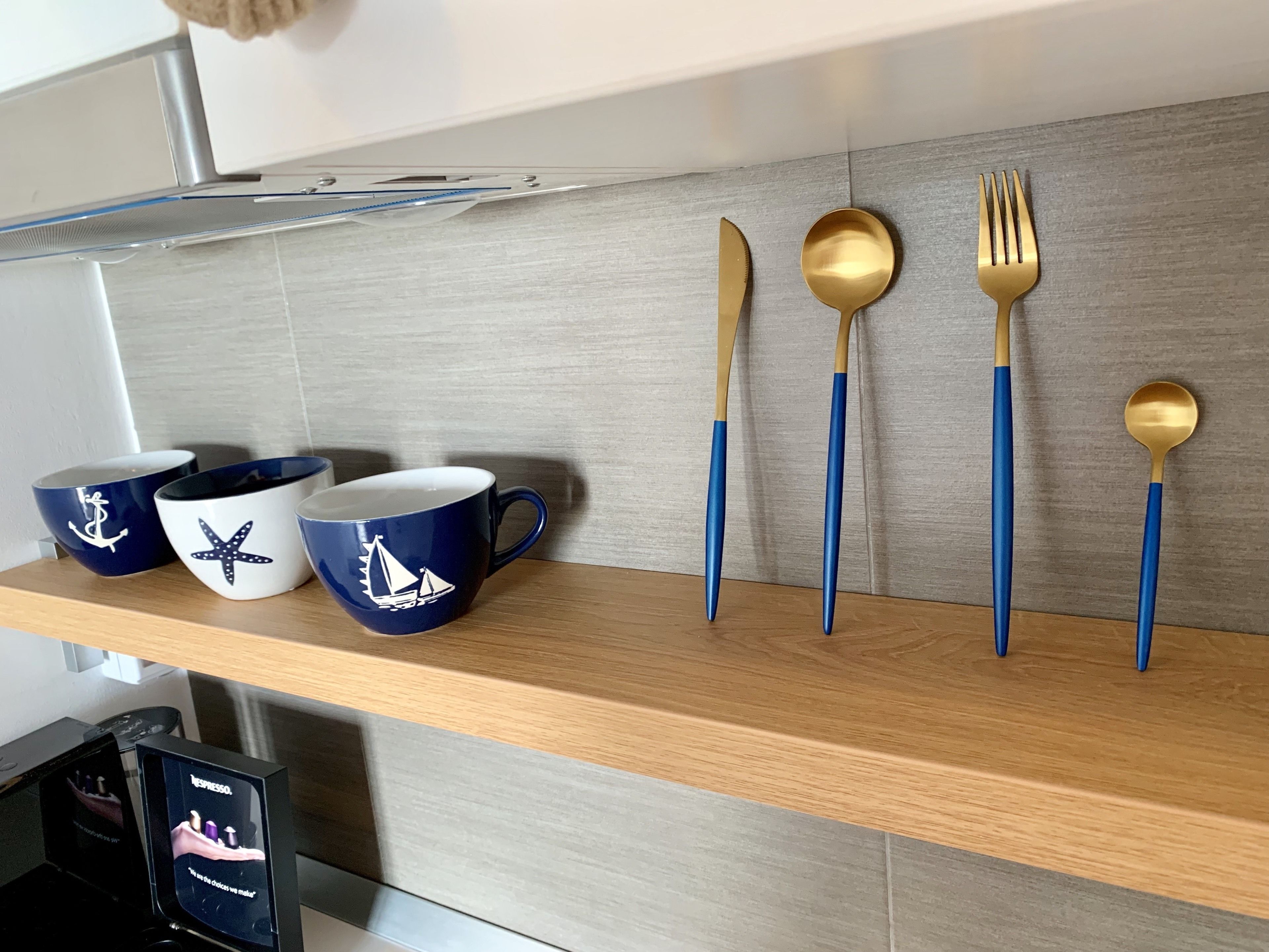 Uno scaffale in cucina con tre tazze blu e bianche, un coltello, un cucchiaio e una forchetta.