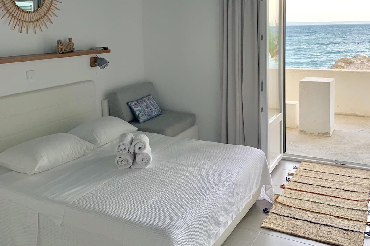 A bedroom with a bed, a bedside table, a mirror, and a view of the sea.