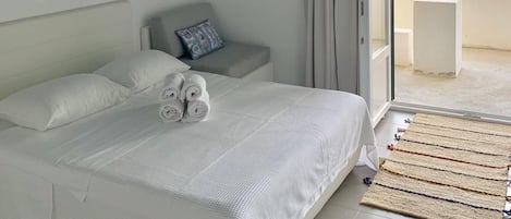 A bedroom with a bed, a bedside table, a mirror, and a view of the sea.