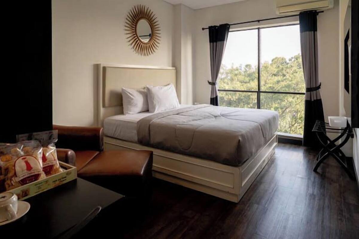 A hotel room with a bed, a desk with a tray of snacks, a mirror, and a window with curtains.